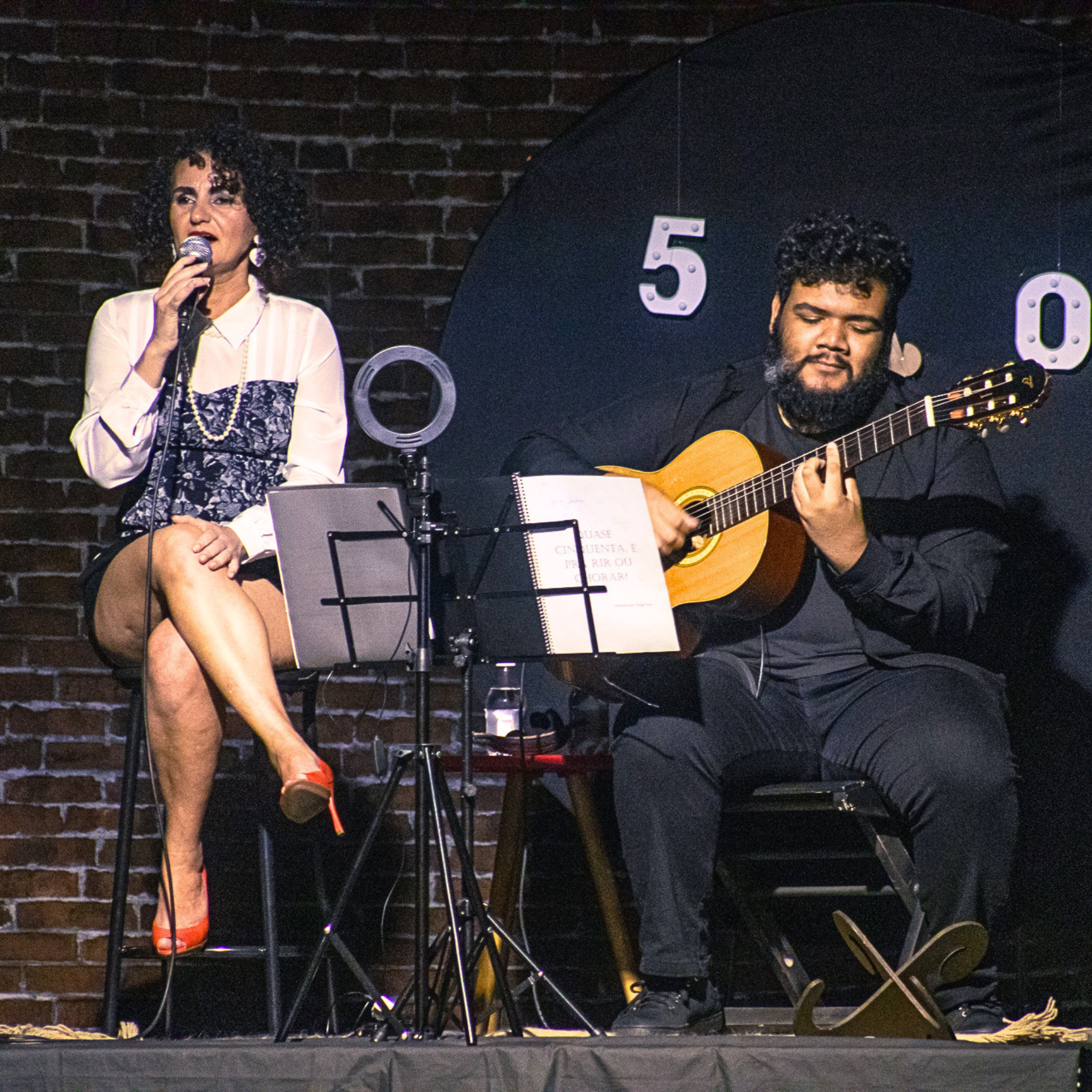 Nellva cantando ao lado de músico com violão
