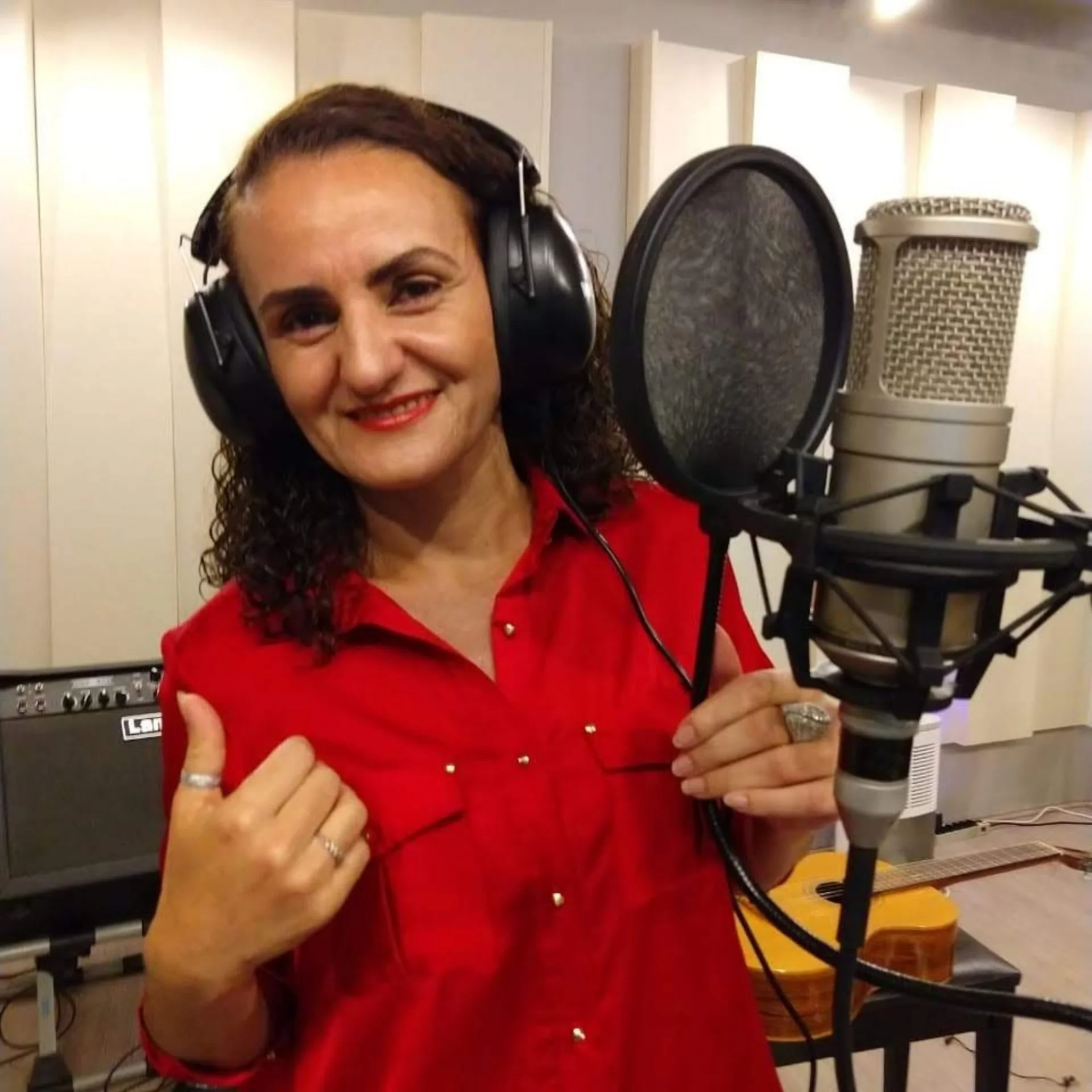 Nellva de camisa vermelha e fones de ouvido ao lado de um microfone de estúdio