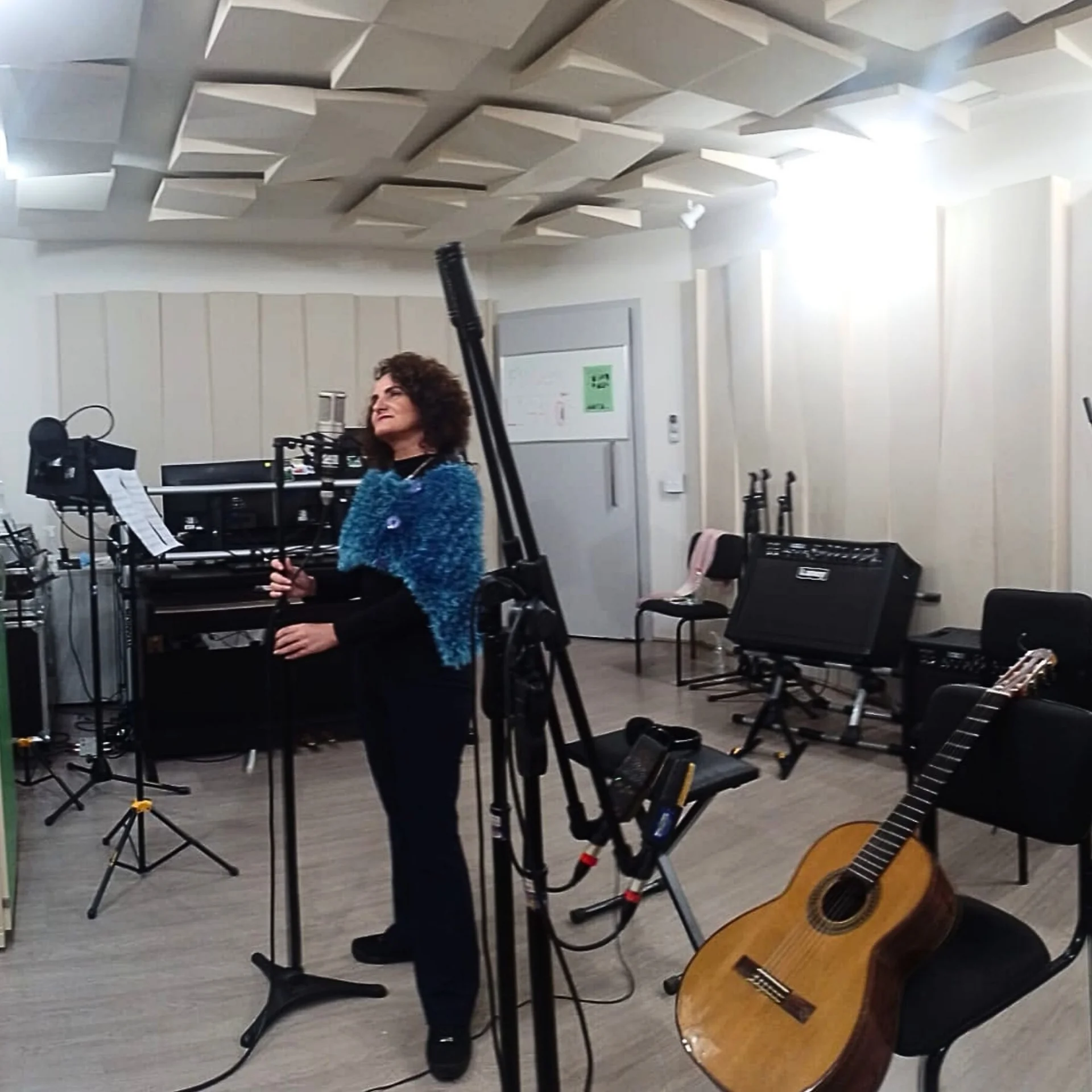 Nellva ao microfone em uma sala com piano, violão e pedestais