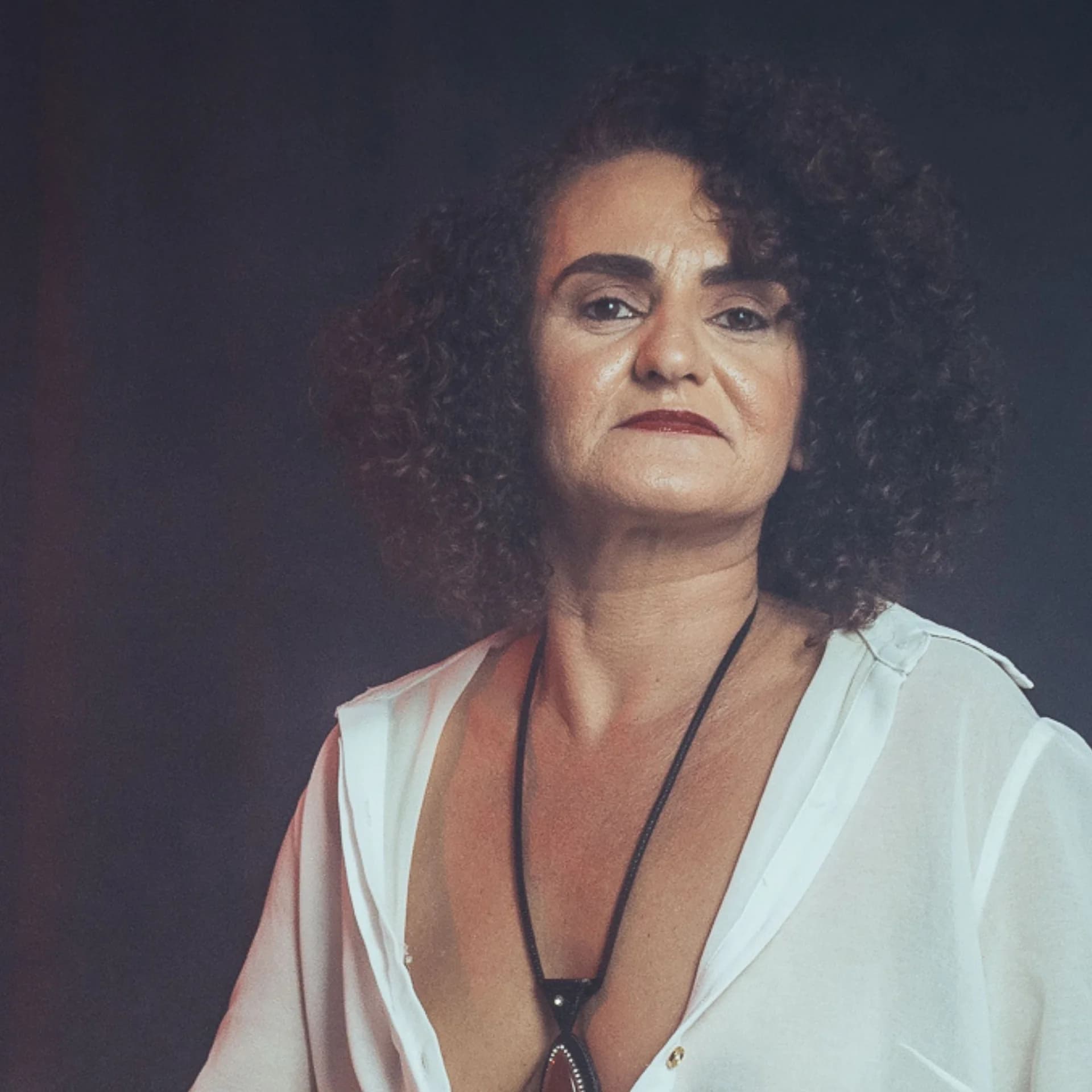 Retrato de Nellva com camisa branca e colar sobre fundo escuro