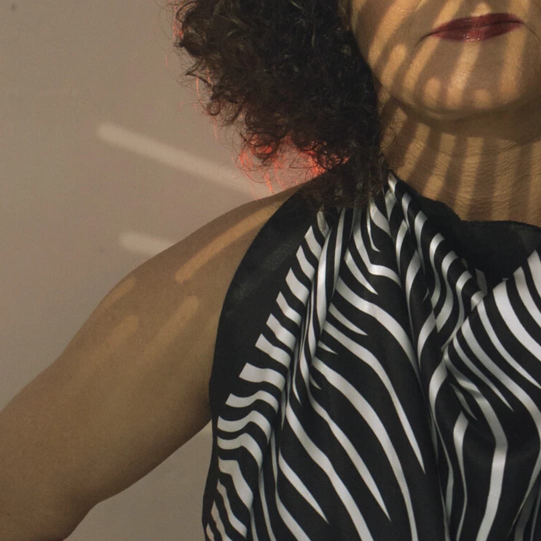 Nellva de perfil, com blusa estampada, sob projeções de luz