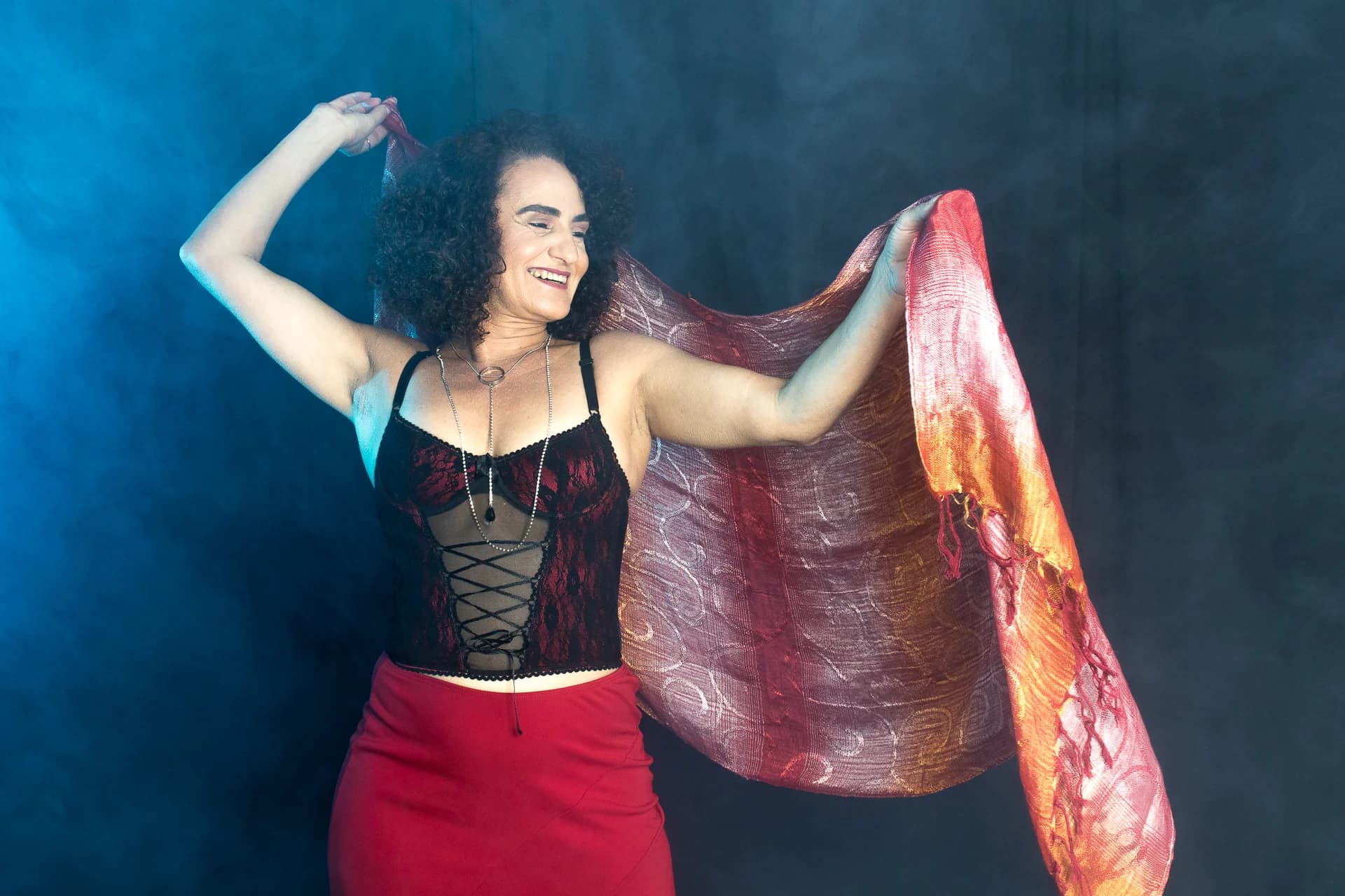 Nellva sorrindo com os braços erguidos e um tecido vermelho e dourado