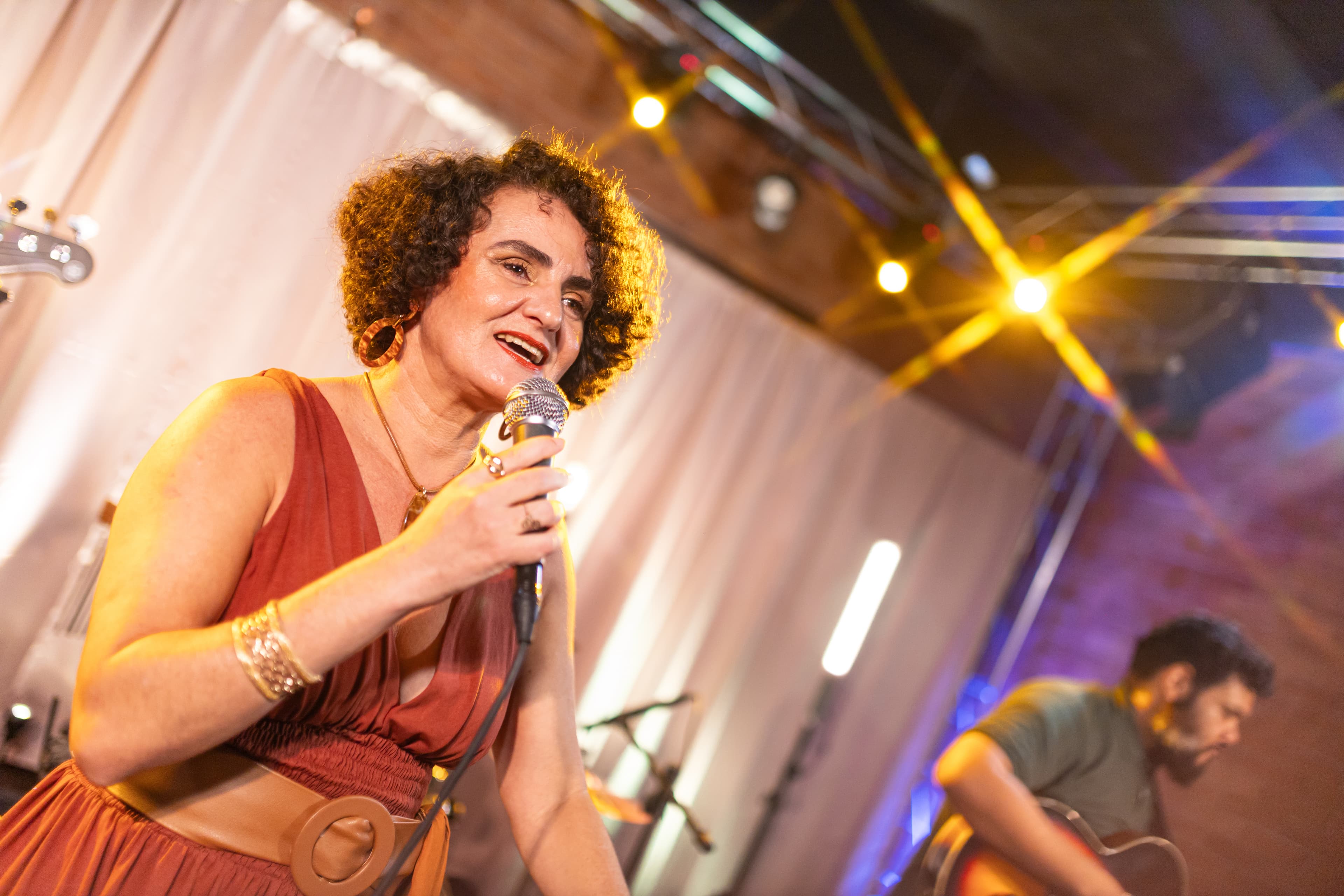 Nellva cantando ao microfone, com violonista ao fundo