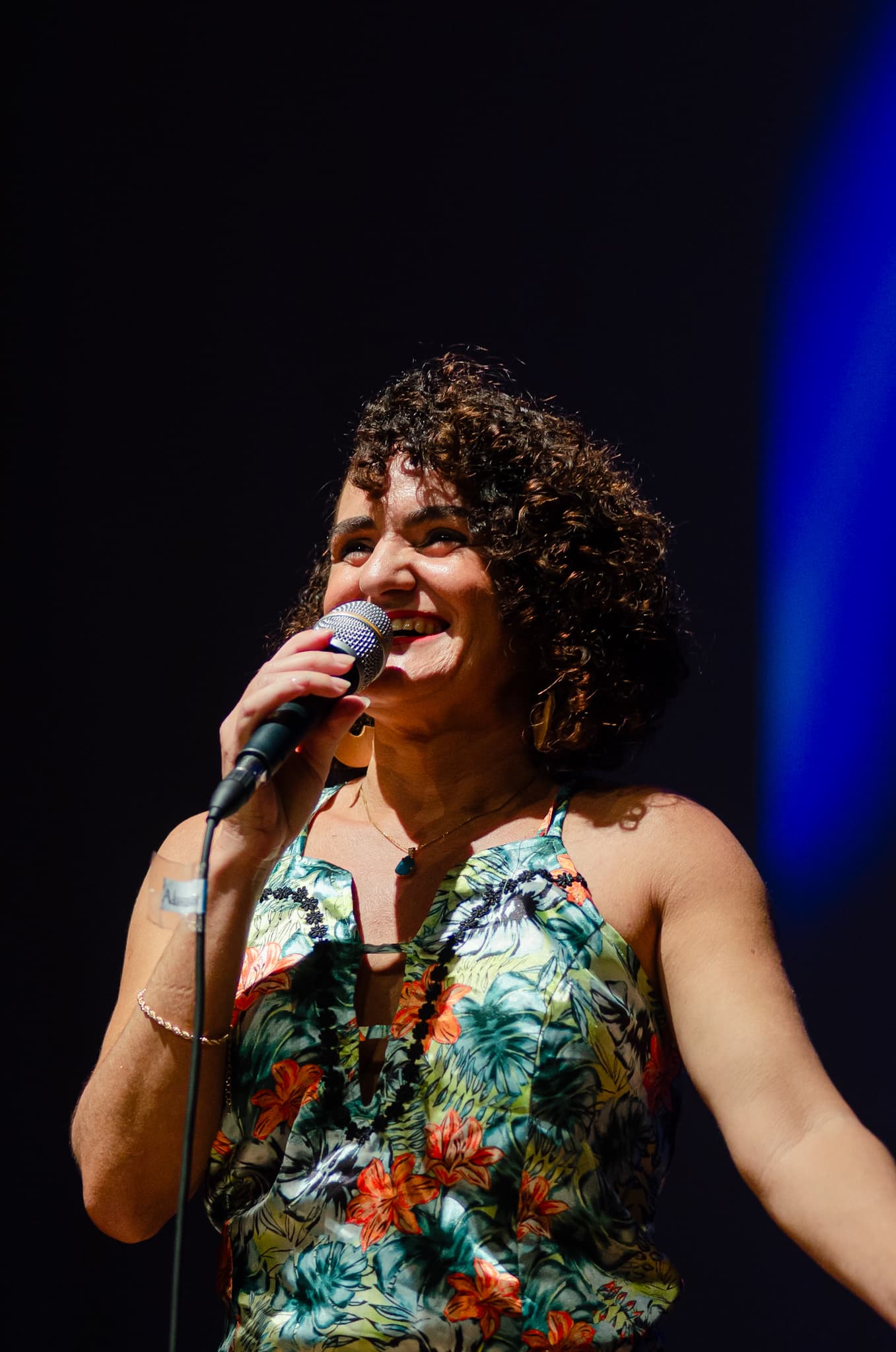 Nellva Sântana cantando ao microfone, de vestido floral