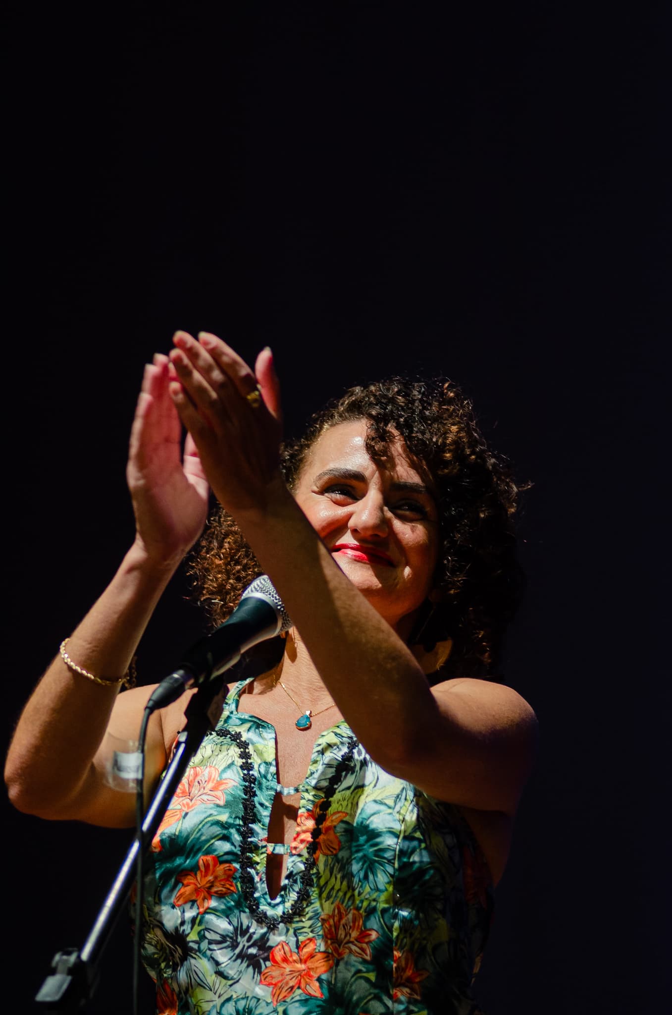 Nellva Sântana sorrindo e aplaudindo diante do microfone
